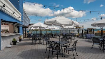 Une terrasse extérieure avec des tables et des chaises, des parasols et un espace bar offrant une vue sur l’eau.