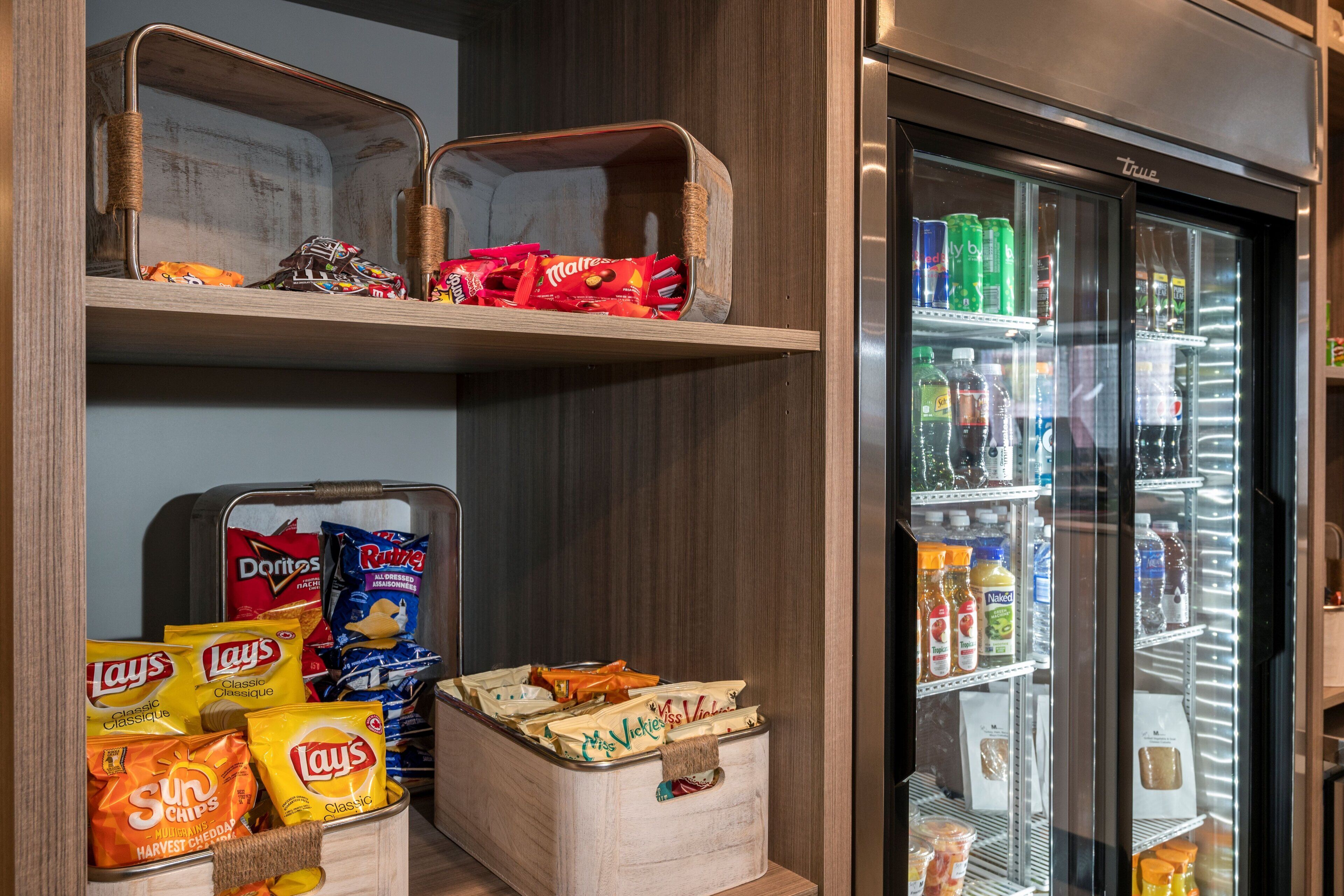 A storage area with shelves holding snacks and a refrigerator stocked with beverages.