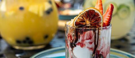 Bebida postre en un vaso con una rodaja de naranja deshidratada y una fresa, servida sobre un plato de vidrio con borde azul.