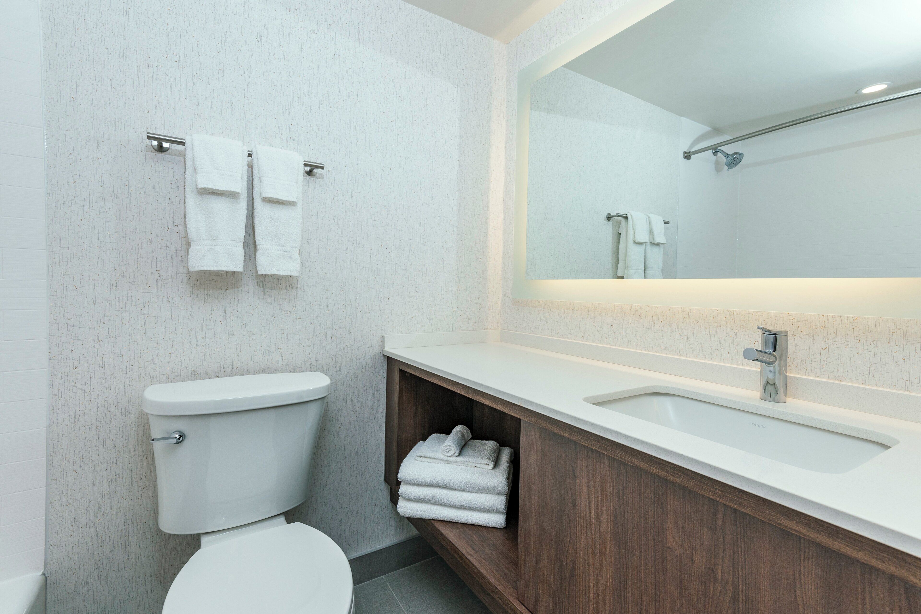 A modern bathroom with a white toilet, a wooden vanity with a sink, and a large mirror.