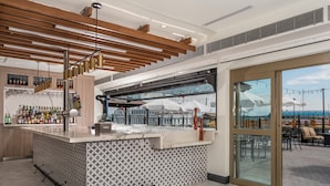 Un espace bar moderne avec un comptoir à motifs, un réfrigérateur à vin et une vue sur l’océan grâce à de grandes fenêtres.