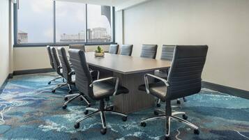 Un salón de conferencias con una mesa larga, seis sillas y una planta en maceta.