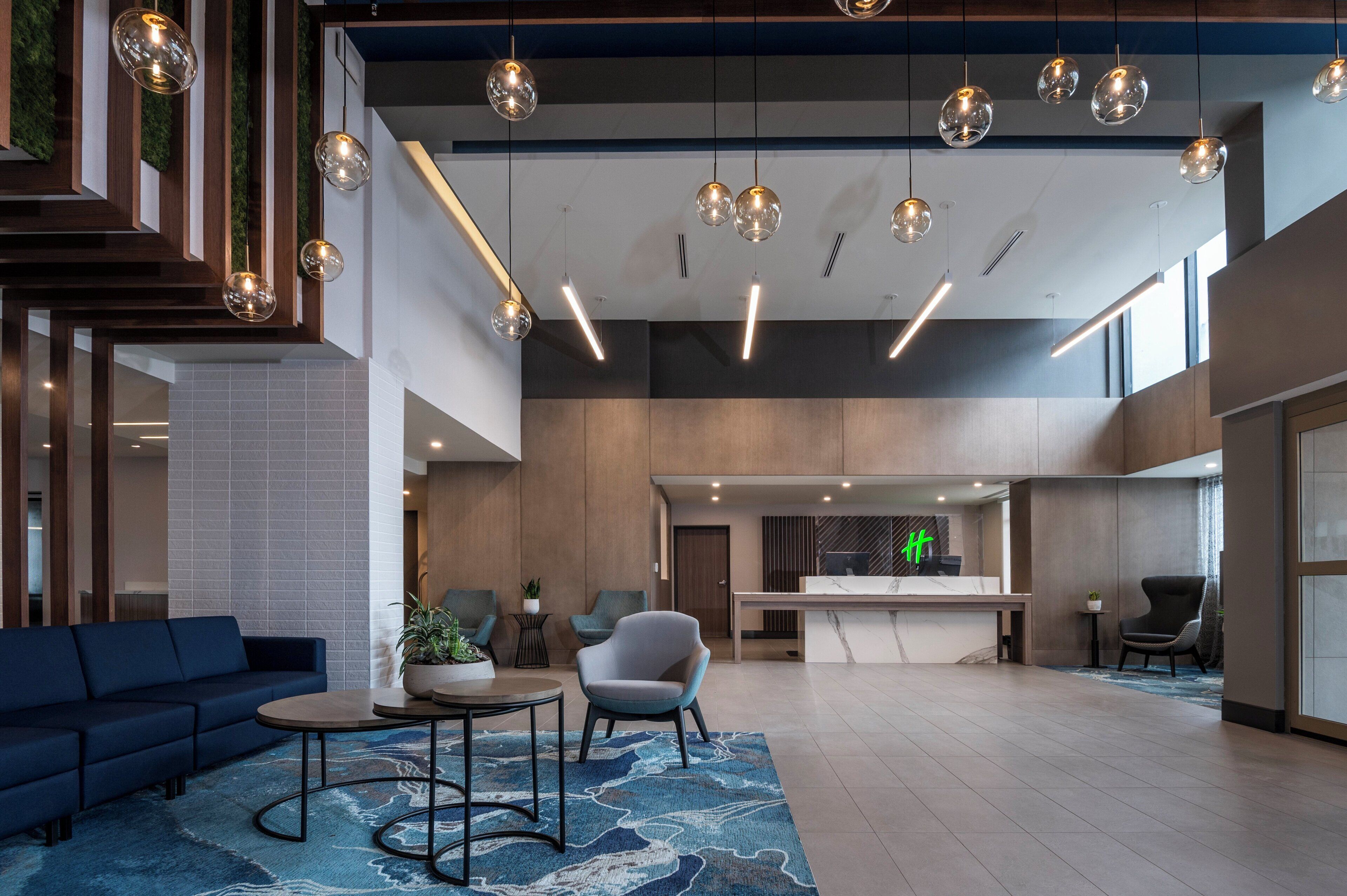 A modern hotel lobby with a reception desk, seating area, and a large open space with a high ceiling and hanging spherical lights.