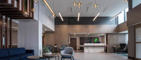 A modern hotel lobby with a reception desk, seating area, and a large open space with a high ceiling and hanging spherical lights.