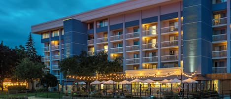 A multi-story hotel with outdoor dining areas and a waterfront view.