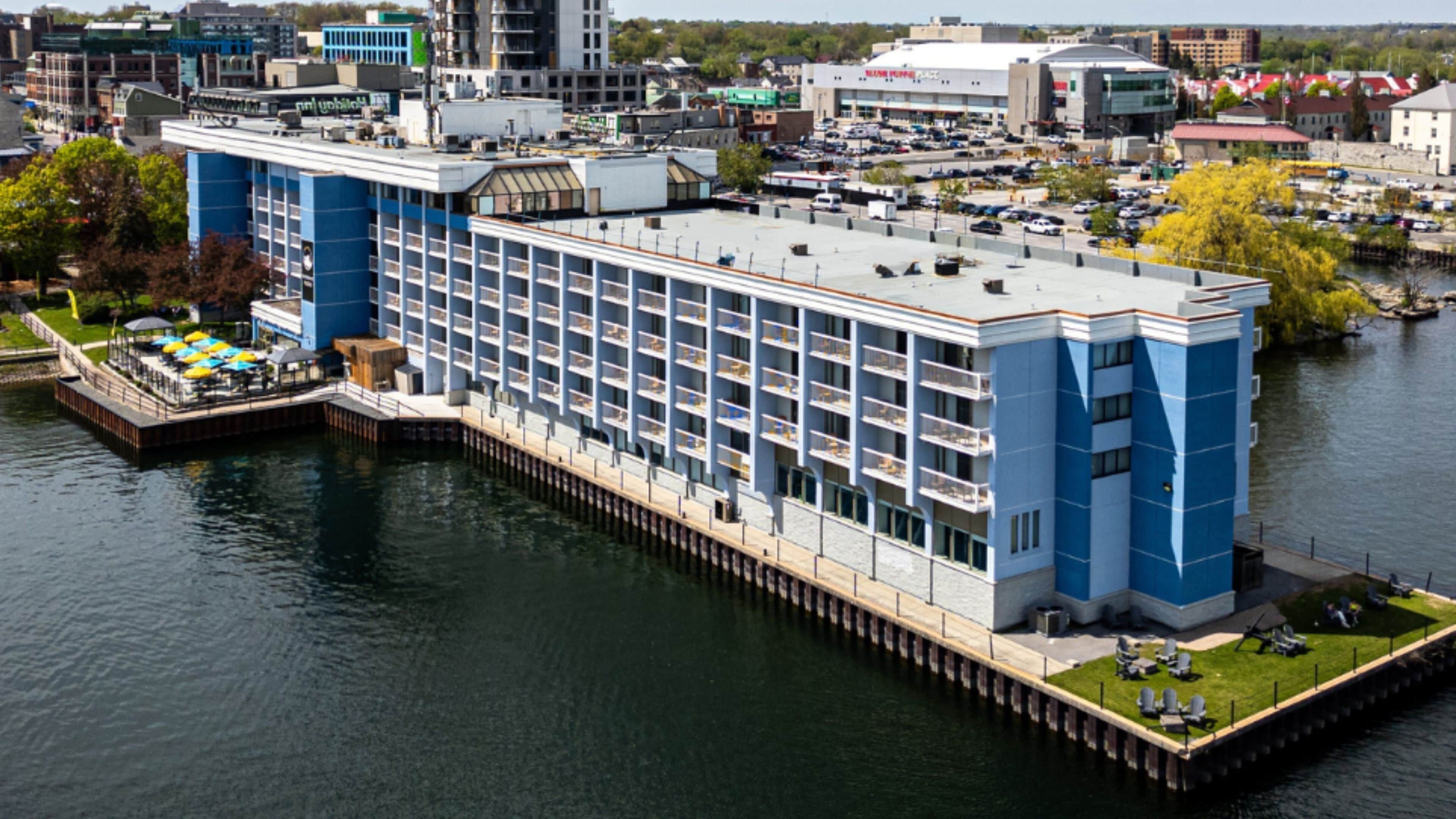 Een hotel aan het water met een steiger, meerdere balkons en uitzicht op de skyline.