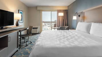 A hotel room with a large bed, a desk with a TV, a chair, a small table, and a view of the city through the window.