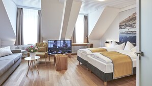 A modern hotel room with a loft bed, a sofa, a TV, and a dining table. - Hotel Central Luzern (Lucerne)