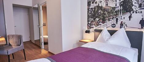 Habitación de hotel con cama, una silla, una mesita de noche y una lámpara fijada en la pared.