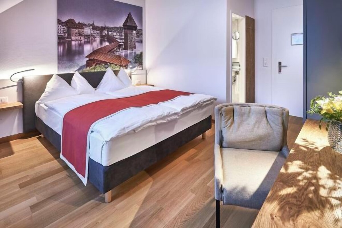 Habitación de hotel con cama, una silla, piso de madera, lámpara de pared y un cartel.