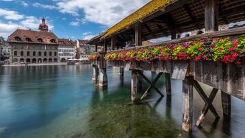A wooden bridge with flower boxes over a calm river, historic buildings in the background, and a clear sky.