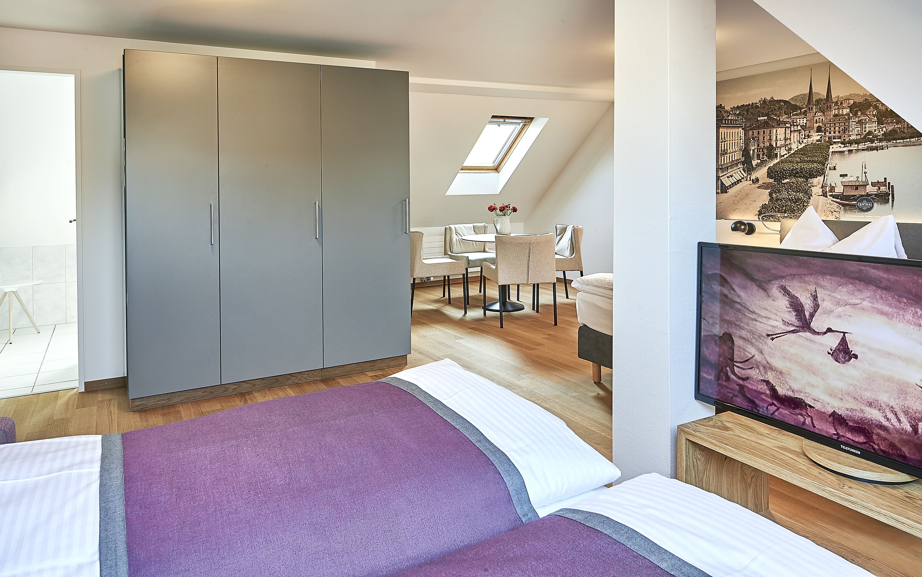 A modern hotel room with a bed, a desk, a chair, and a large wardrobe.