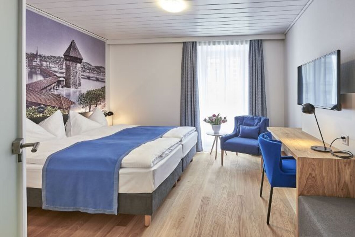 A hotel room with a bed, a desk, a chair, a TV, and a window with curtains.