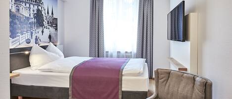 Habitación de hotel con cama, una silla, televisor y un ventanal con cortinas.