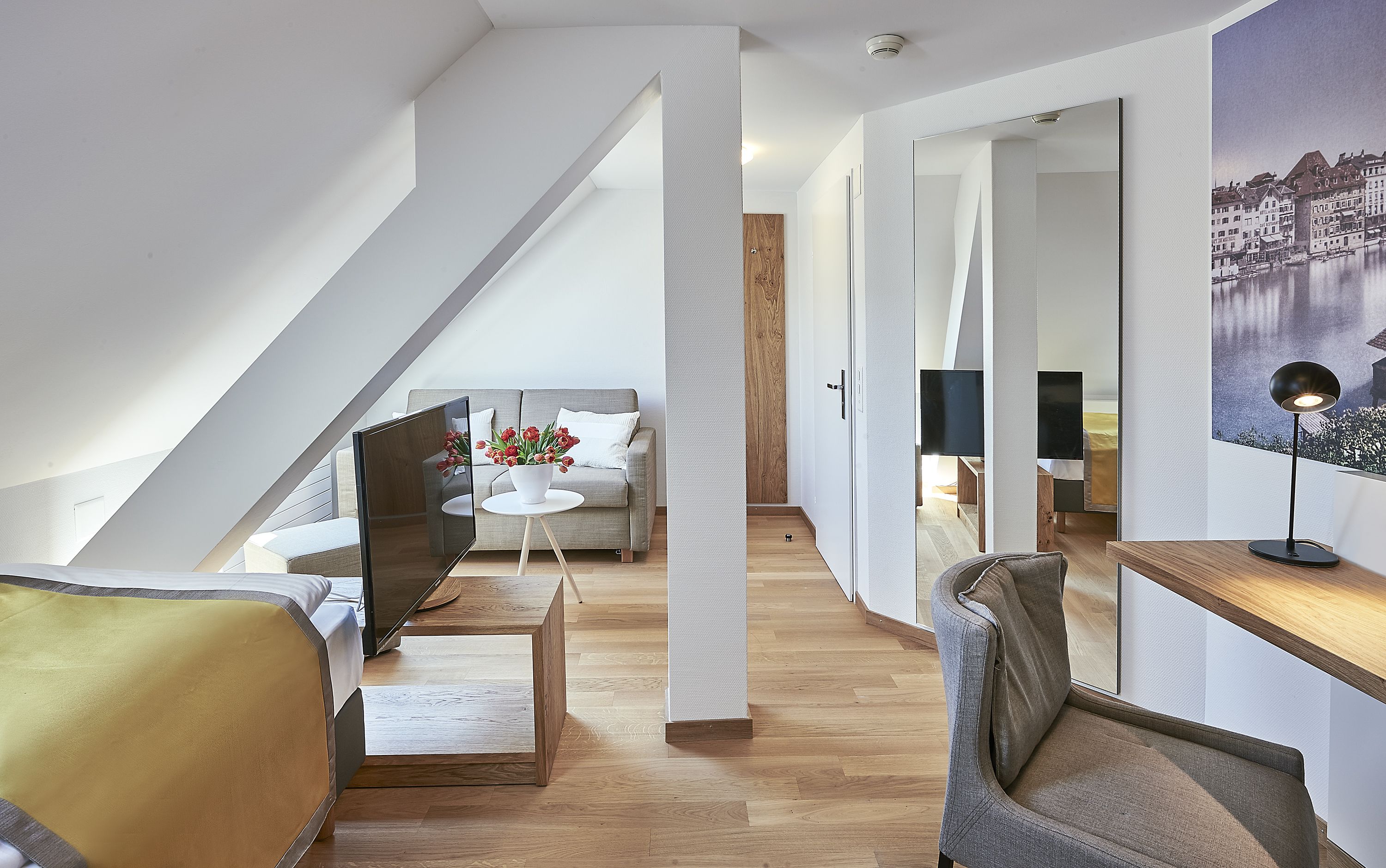 A modern loft bedroom with a sloped ceiling, a large window, a bed, a desk, and a chair.