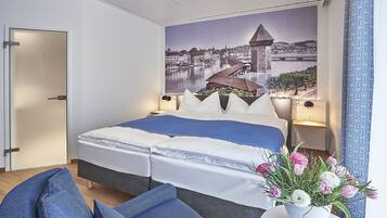 Ein Schlafzimmer mit Bett, Kissen, Nachttisch, Lampe, einem Wandbild und einer Vase mit Blumen.