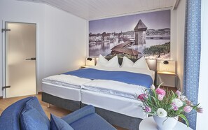 A bedroom with a bed, pillows, a nightstand, a lamp, a wall-mounted picture, and a vase with flowers. - Hotel Central Luzern (Lucerne)