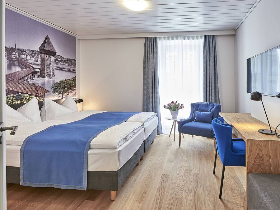 Una habitación de hotel con cama, escritorio, silla, televisión y un mural en la pared.