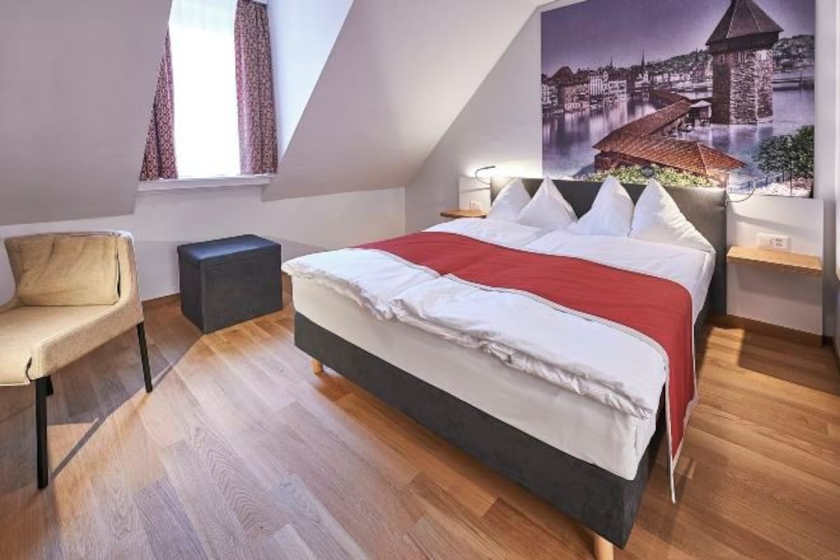 A bedroom with a bed, a chair, a nightstand, and a painting of a castle on the wall.