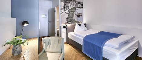 Una habitación de hotel moderna con una cama, una silla, un escritorio con lámpara y un mural grande en la pared.