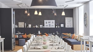 A modern dining area with a long table set for a meal, a sofa with cushions, and pendant lighting. - Hotel Central Luzern (Lucerne)