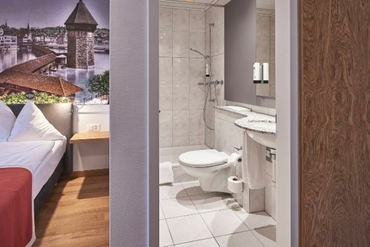 A hotel room with a bed, a bathroom with a toilet, and a view of a cityscape.