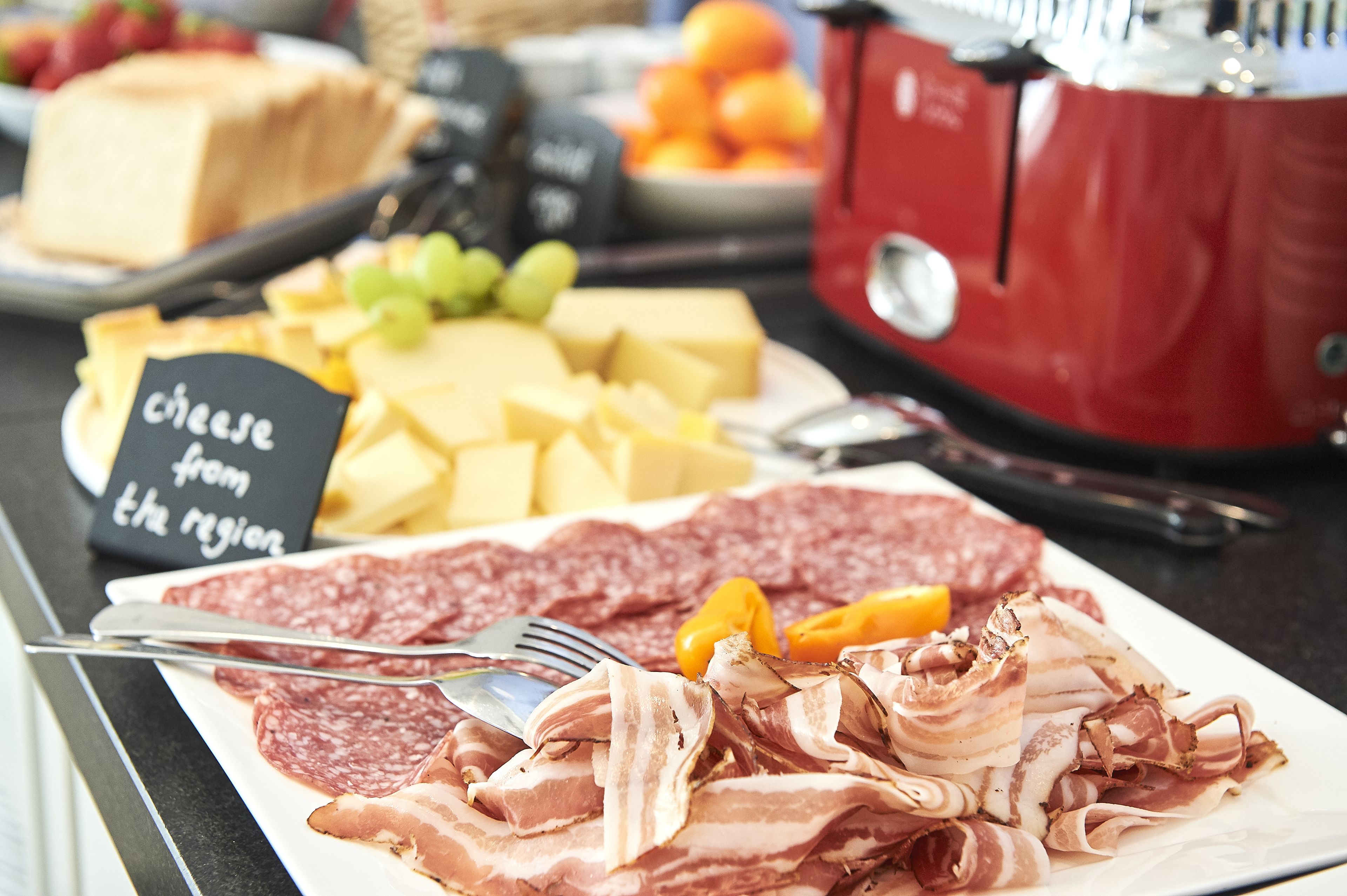 Un bufé con diversos quesos, carnes y frutas.