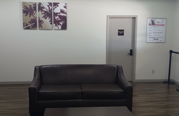 A room with a dark brown leather sofa, a door with an 'EMPLOYEES ONLY' sign, and a poster on the wall. - Red Roof Inn Fort Worth West (Fort Worth)