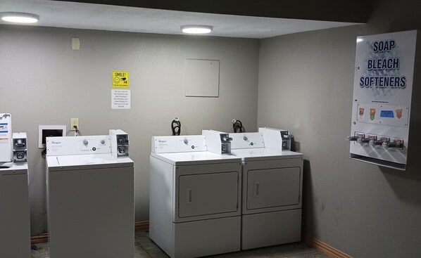 A laundry room with Whirlpool washers and dryers, a sign listing soap, bleach, and softeners, and a 'Smile! You're on camera' sign. - Red Roof Inn Fort Worth West (Fort Worth)