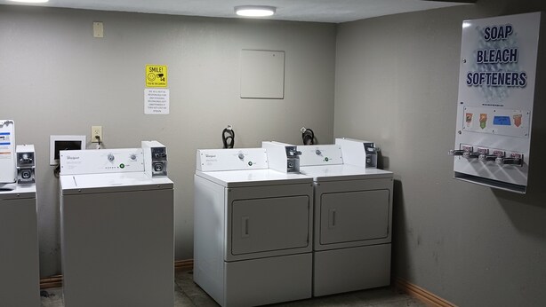 A laundry room with Whirlpool washers and dryers, a sign for soap, bleach, and softeners, and a 'Smile! You're on camera' sign. - Red Roof Inn Fort Worth West (Fort Worth)