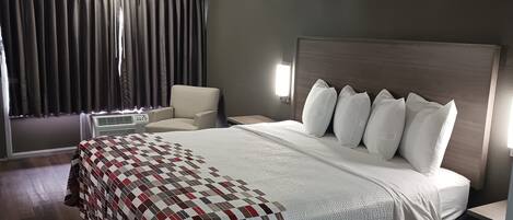 A hotel room with a large bed, a chair, a bedside table, and a window with curtains.