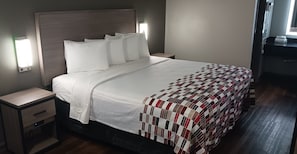 A neatly made bed with a quilt, a bedside table with a drawer, and a wall-mounted light fixture. - Red Roof Inn Fort Worth West (Fort Worth)