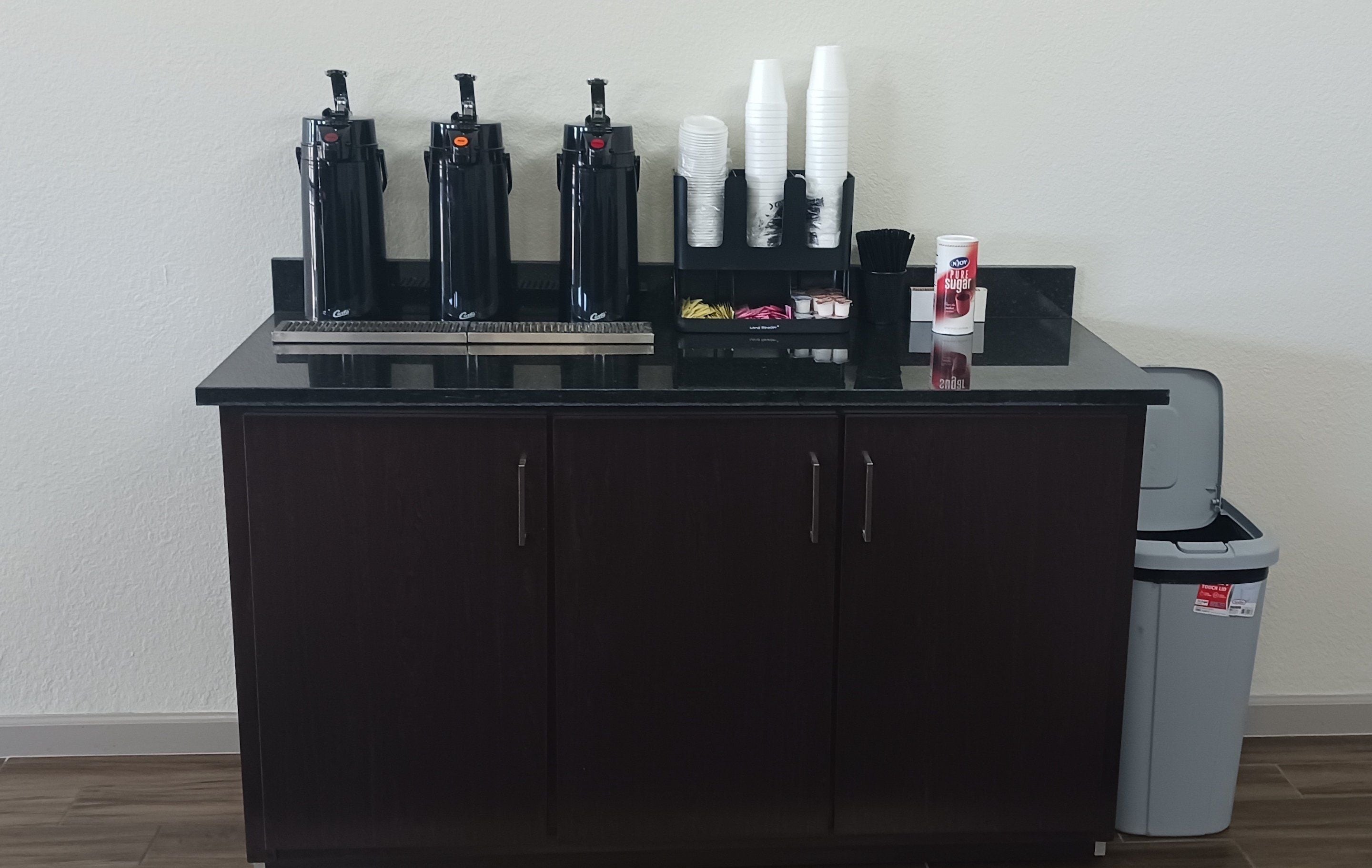 A bar area with a black countertop, multiple bottles, and a trash bin.