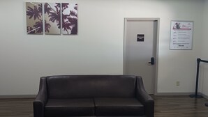 A room with a dark brown leather sofa, a door with an 'EMPLOYEES ONLY' sign, and a framed informational poster on the wall. - Red Roof Inn Fort Worth West (Fort Worth)