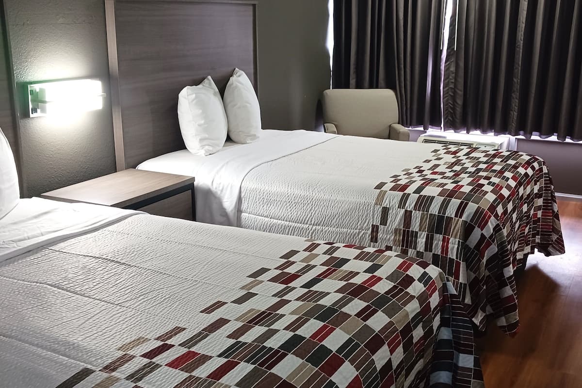 Een hotelkamer met twee bedden, een nachtkastje, een stoel en een raam met gordijnen.