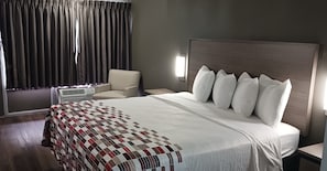 A hotel room with a large bed, a chair, a bedside table, and a window with curtains.