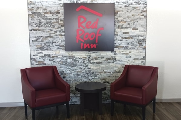 Cartell de Red Roof Inn sobre una paret amb relleu, dues cadires vermelles i una taula rodona petita.