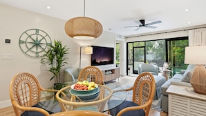 A modern living room with a glass dining table, wicker chairs, a TV, and a large window. - Park Shore Resort (Naples)