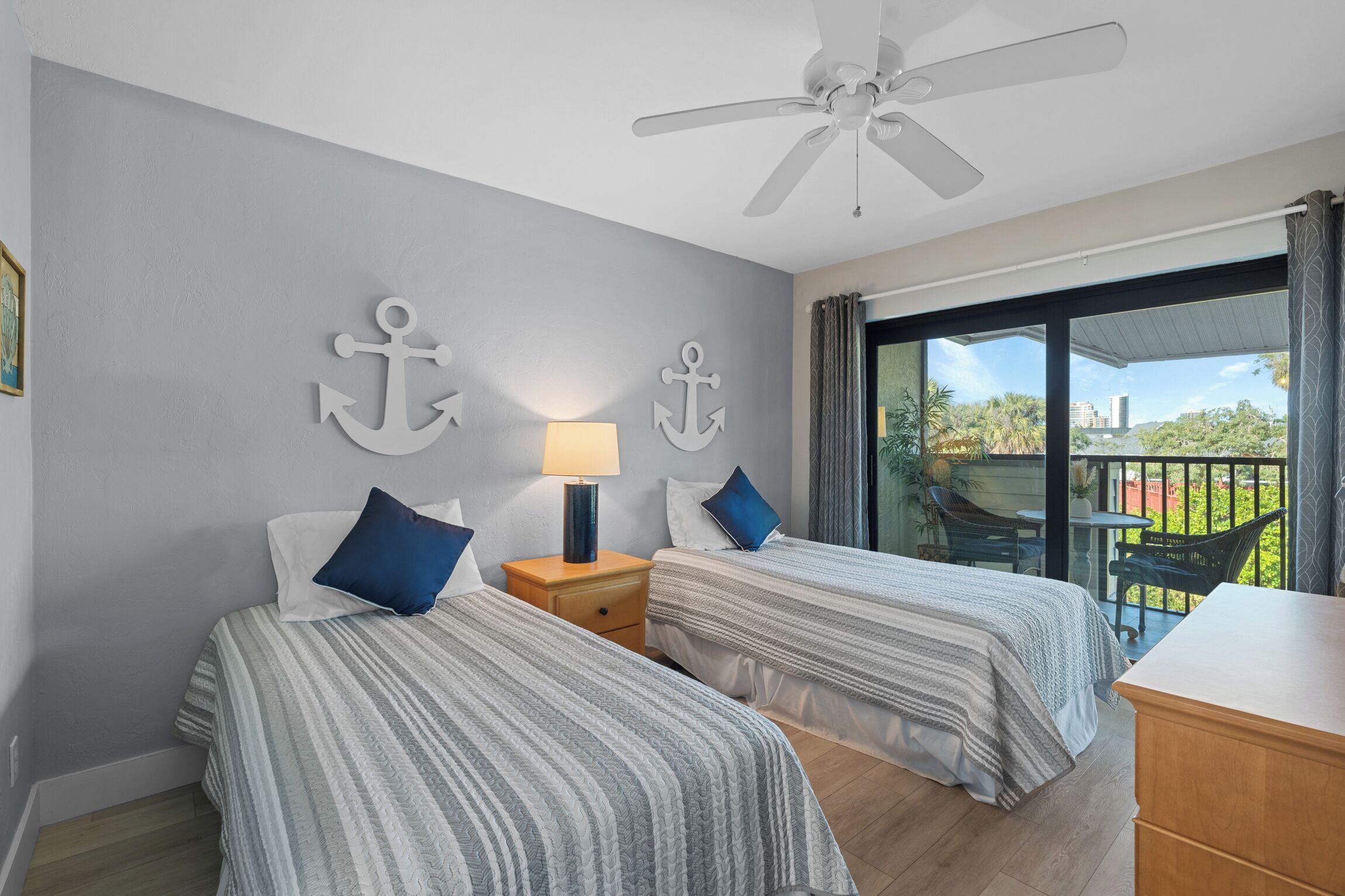 A hotel room with two beds, a ceiling fan, a balcony with a table and chairs, and a view of the outside.