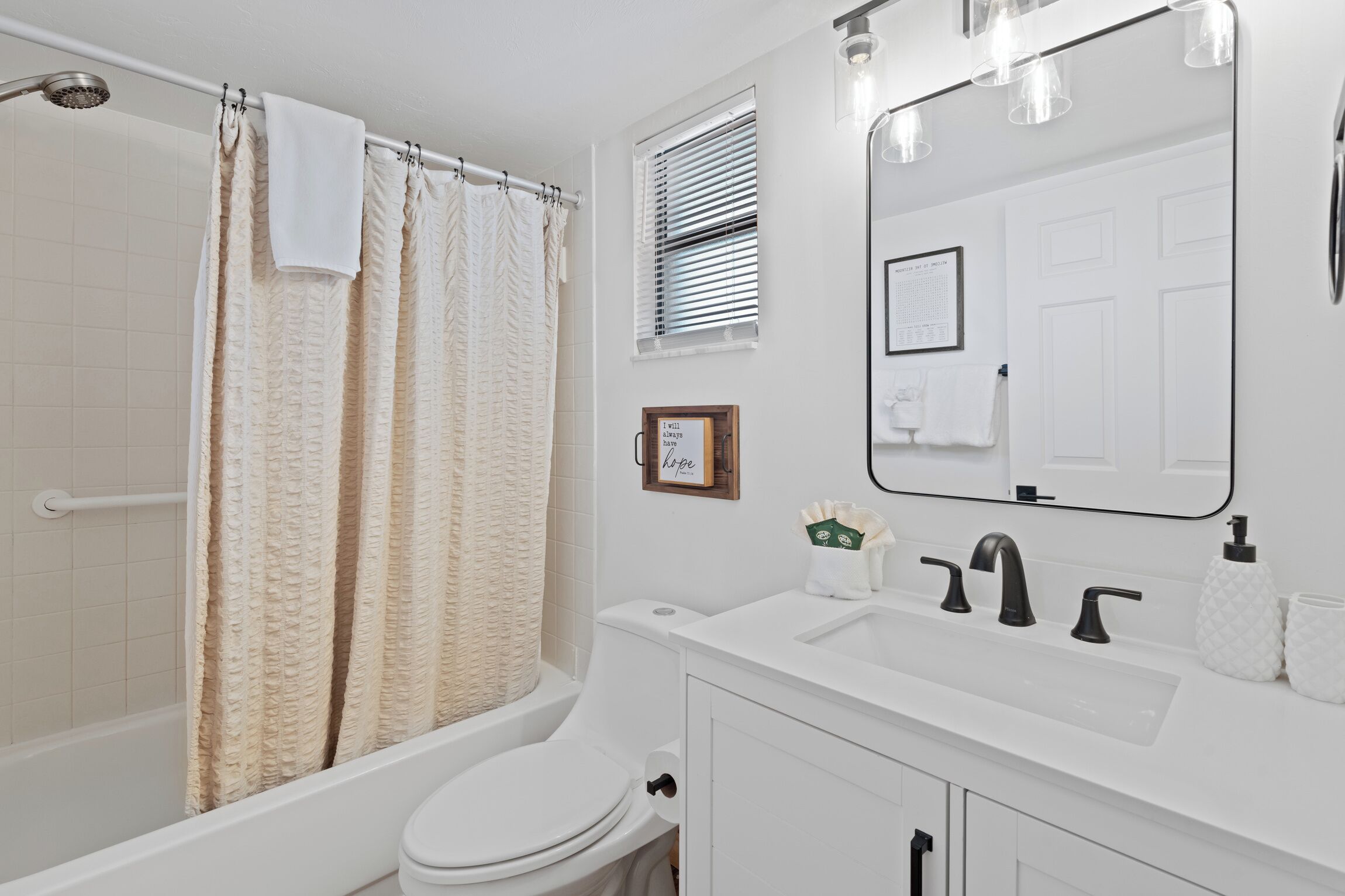 A bathroom with a bathtub, toilet, sink, and a large mirror.