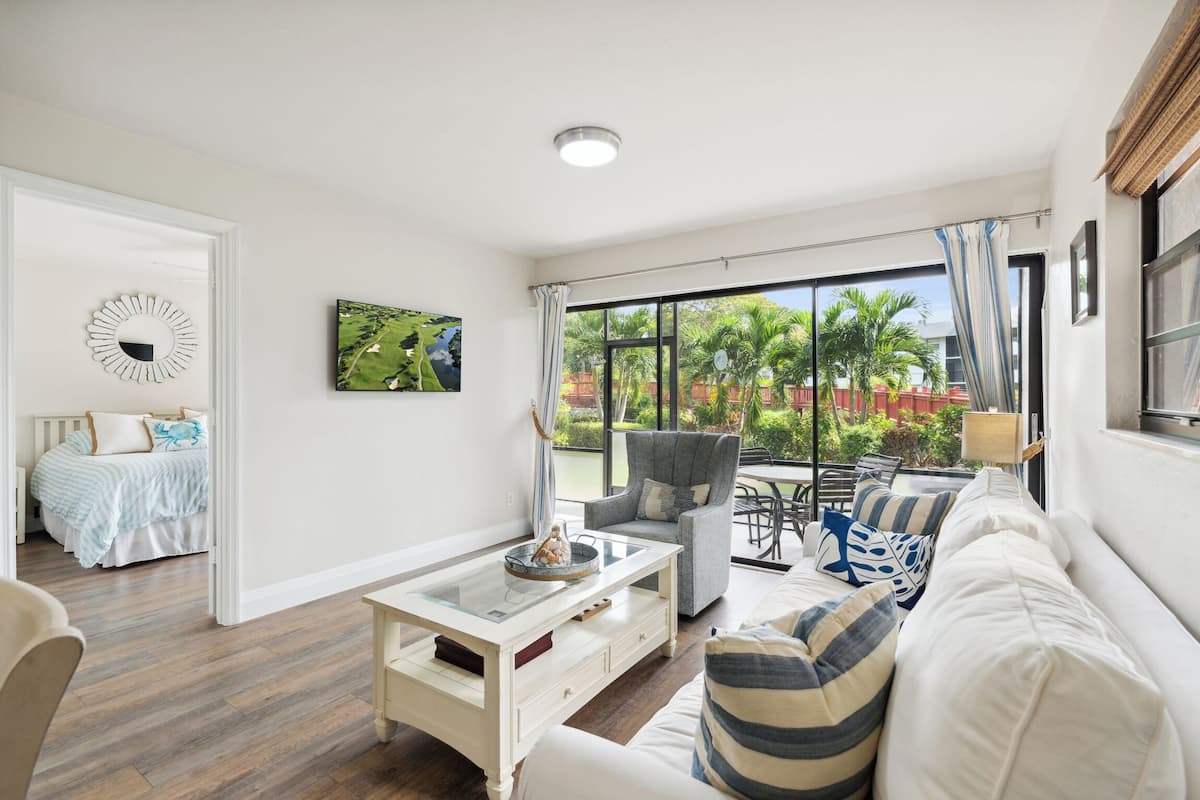 A spacious living room with a large window, a sofa, a coffee table, and a chair.