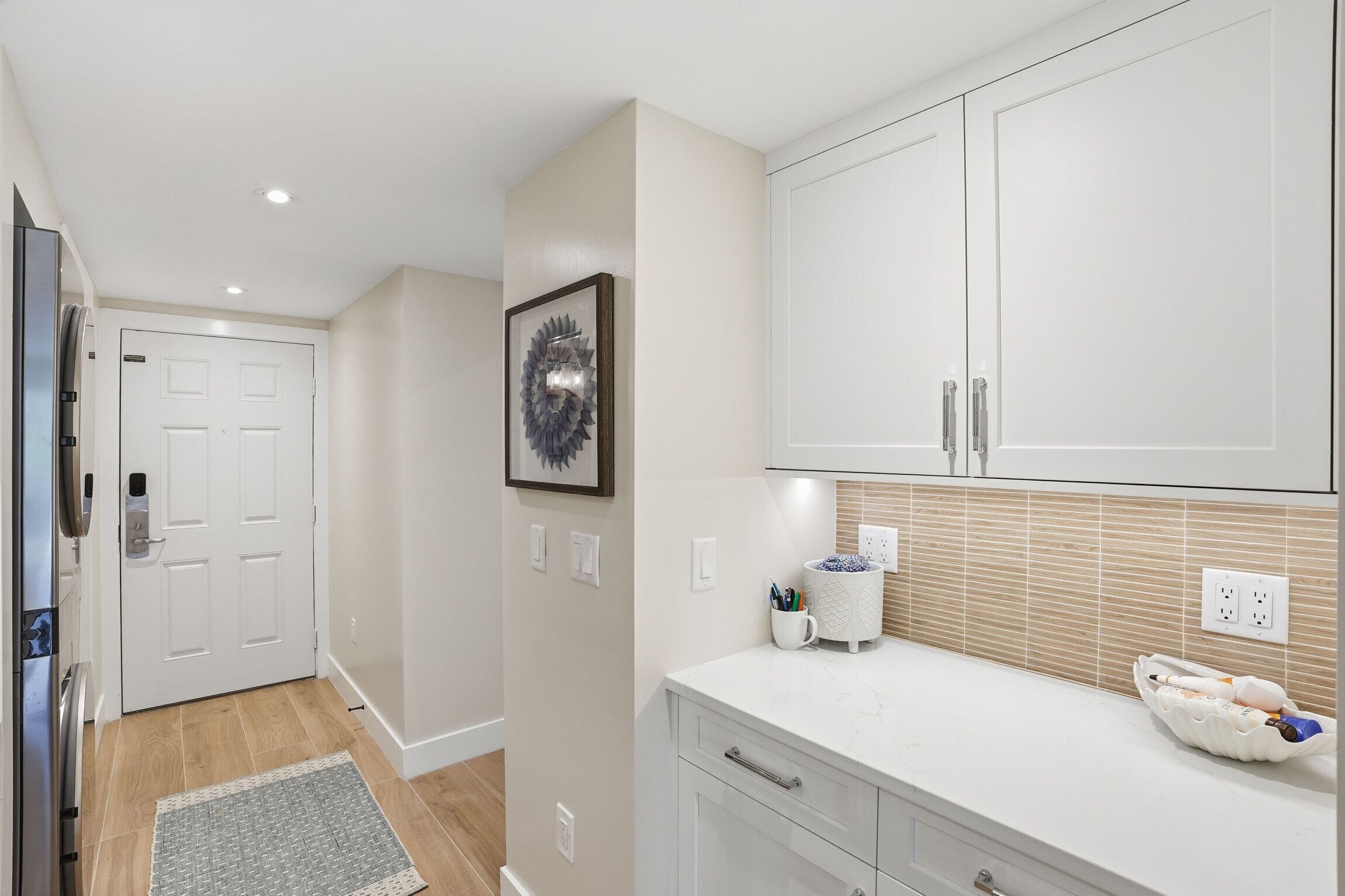 A modern kitchen with white cabinetry, a framed artwork on the wall, and a countertop with a mug and pens.