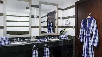 A bathroom with two sinks, a large mirror, a robe hanging on the door, and towels on the counter.