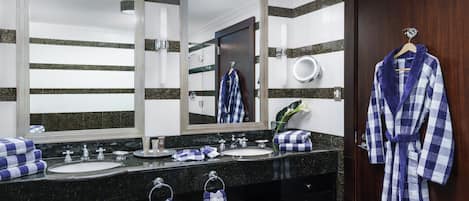 A bathroom with two sinks, a large mirror, a robe hanging on the door, and towels on the counter.