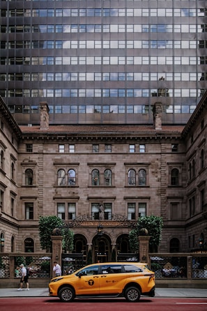 A yellow taxi in front of a historic building with a large glass facade and a classic entrance.