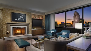 A modern living room with a fireplace, comfortable seating, a coffee table, and a large window with a city view. - Lotte New York Palace (New York)
