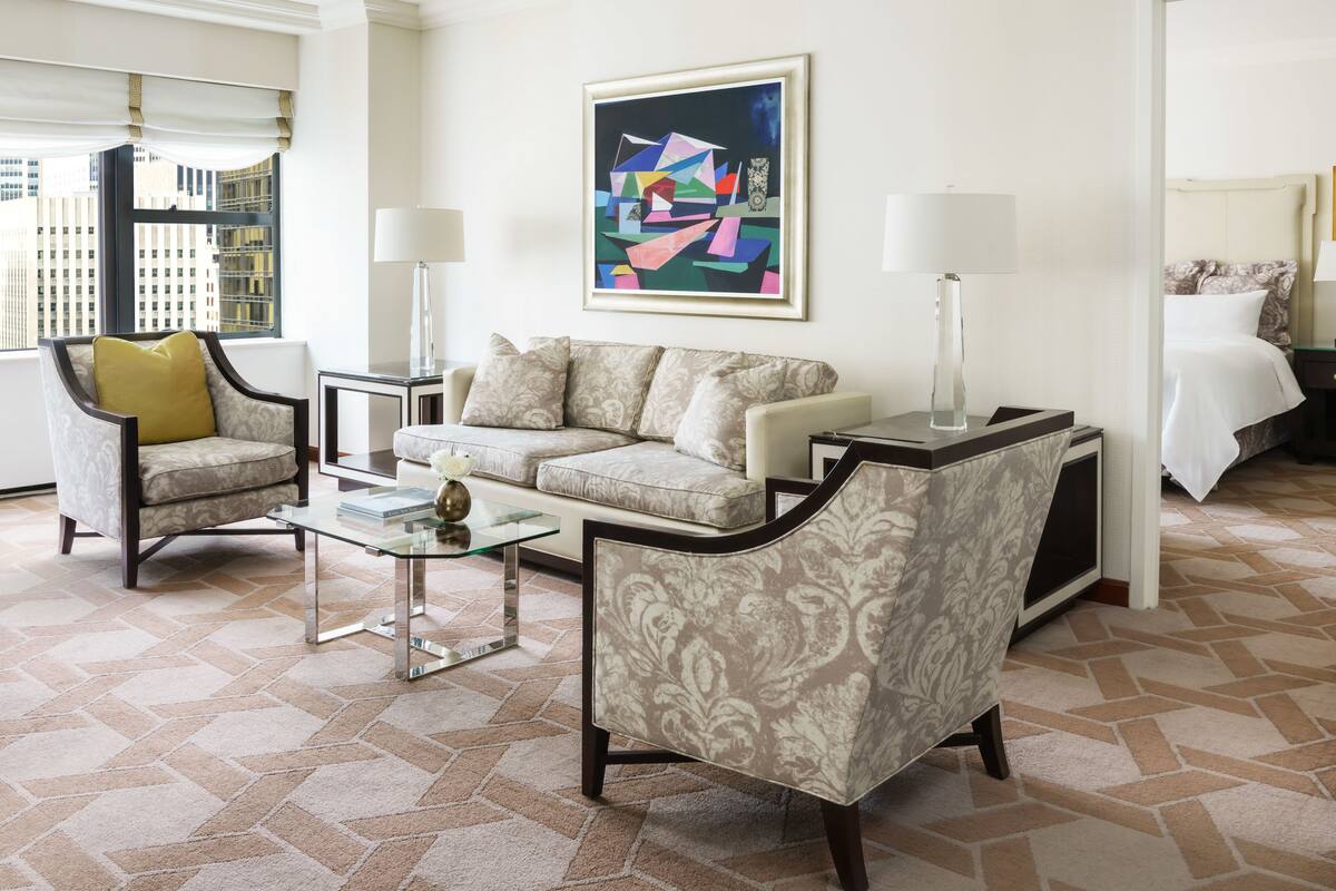 Een moderne hotelkamer met een bank, fauteuils, een glazen salontafel en een schilderij aan de muur.
