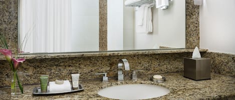 Un baño con encimera de granito, lavamanos, espejo, toallero y cortina de ducha.