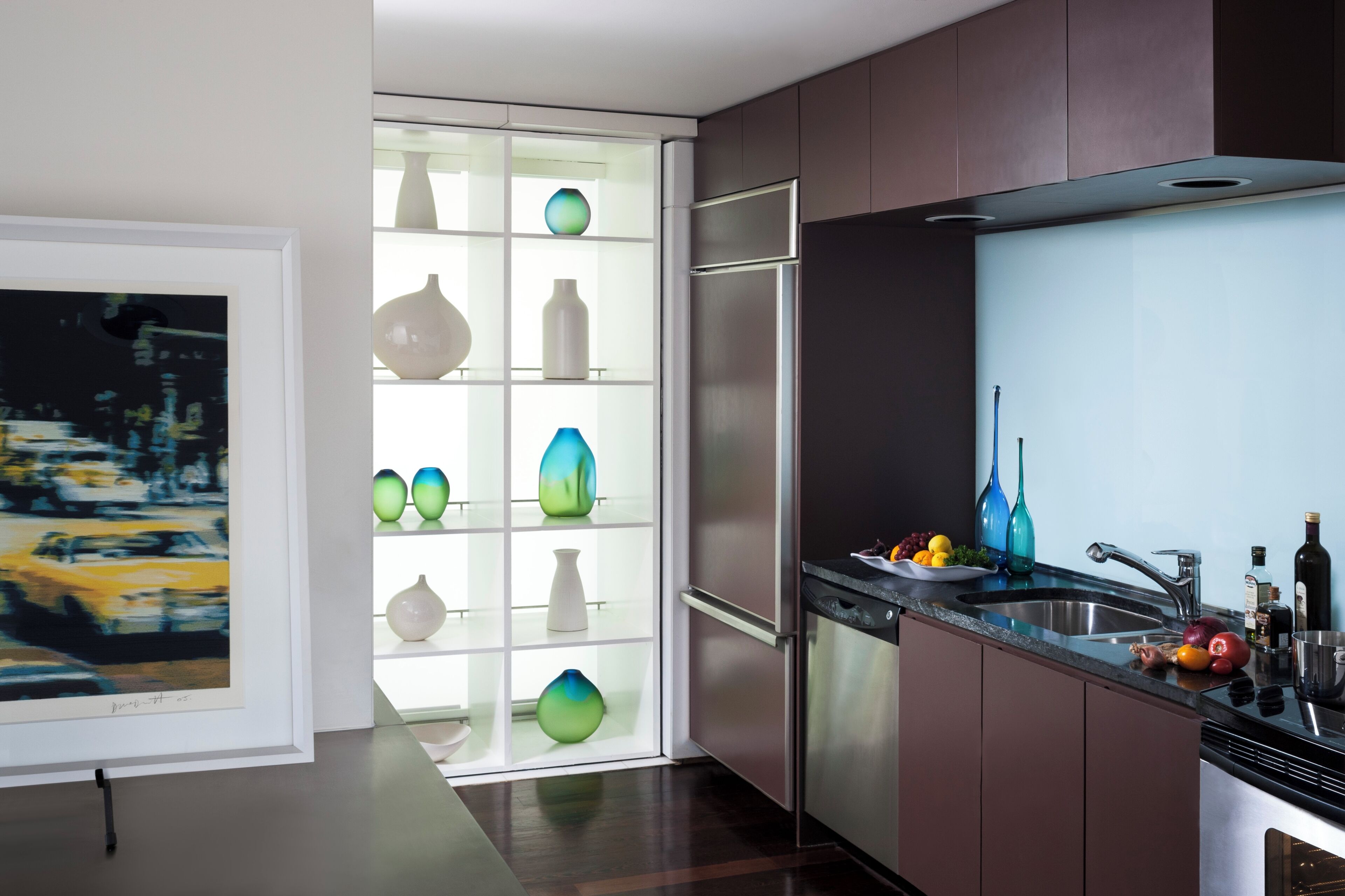 A modern kitchen with a built-in dishwasher, stainless steel appliances, and a glass-fronted display cabinet with decorative vases.