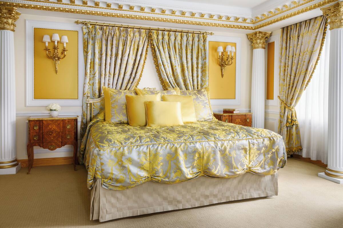 Een luxueuze slaapkamer met een groot bed, sierlijke gordijnen en gouden accenten.